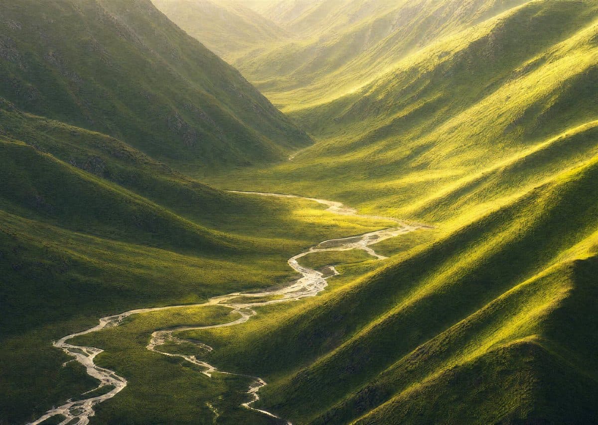 A river winding safely through a green valley between two hills